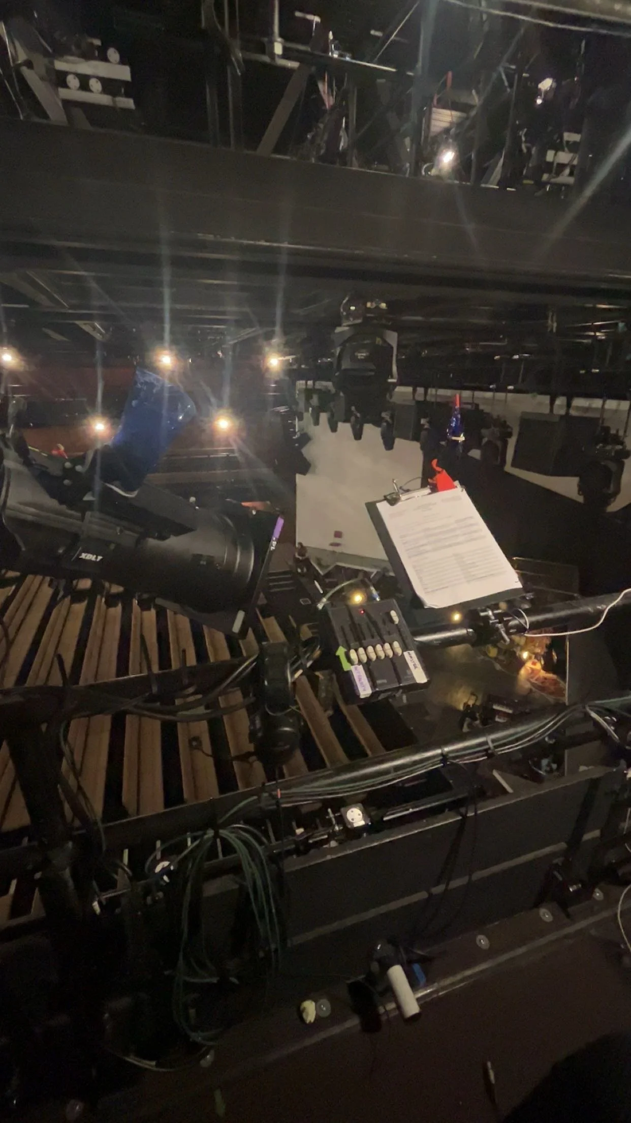 Photo of a stage or theater setup with lighting and equipment, including a clipboard attached to a bicycle handlebar and various cables and devices.