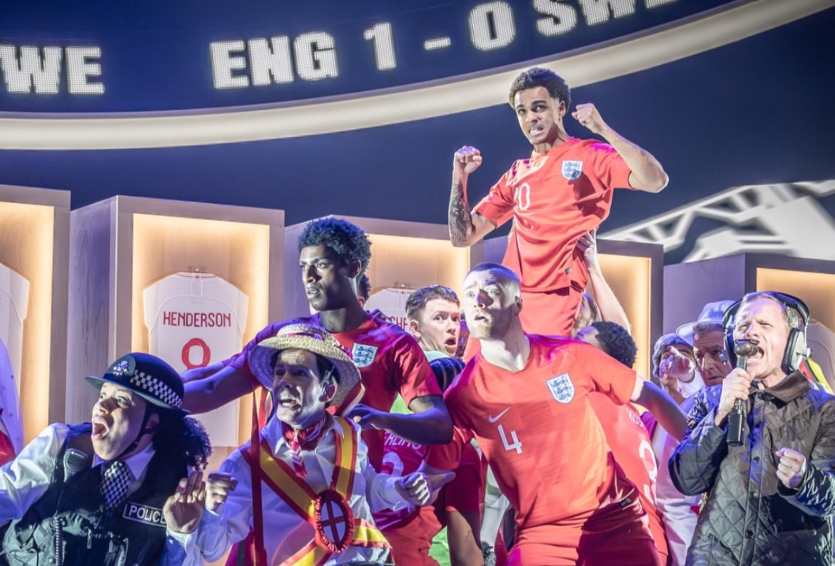 English soccer players celebrating on the field after a match, with a scoreboard in the background showing England's score as 1, opposition score as 0, and a man in a police costume.