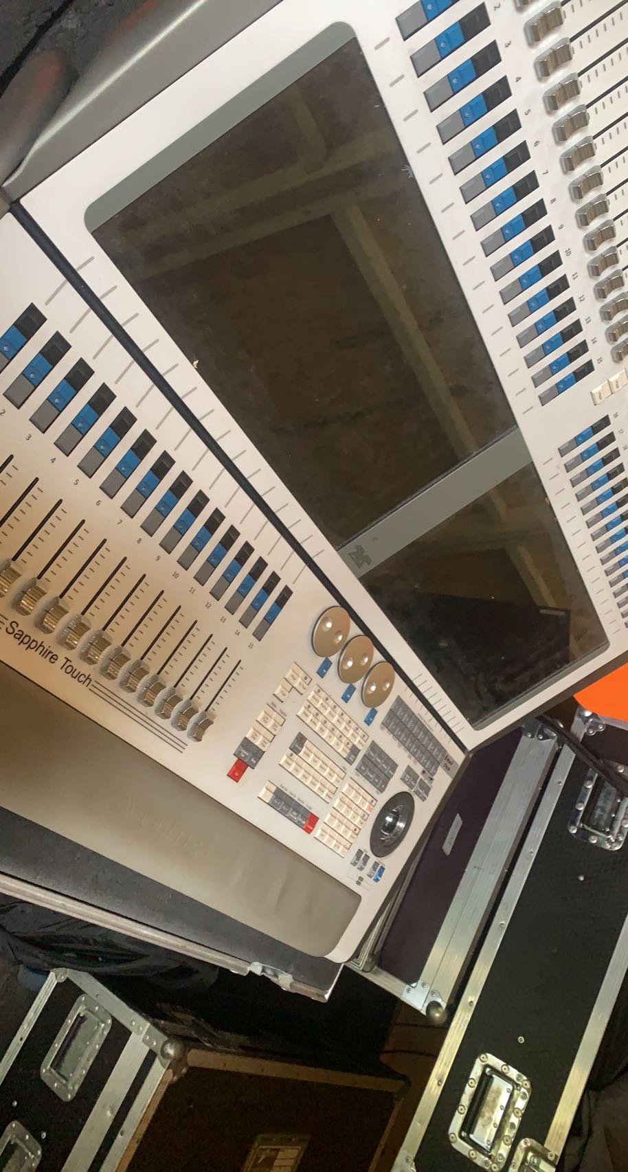 A professional lighting console with multiple faders, knobs, and buttons, used for light programming.