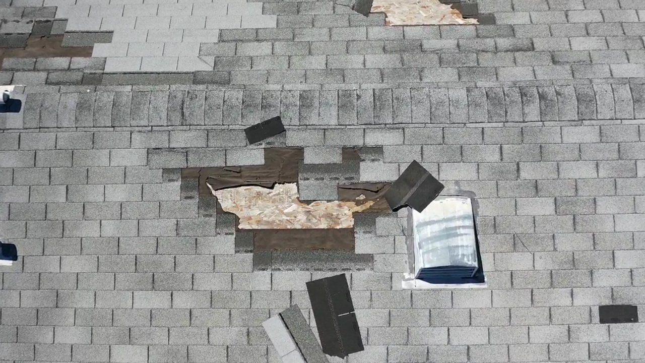 Lifted and displaced three-tab asphalt shingles on a residential roof.