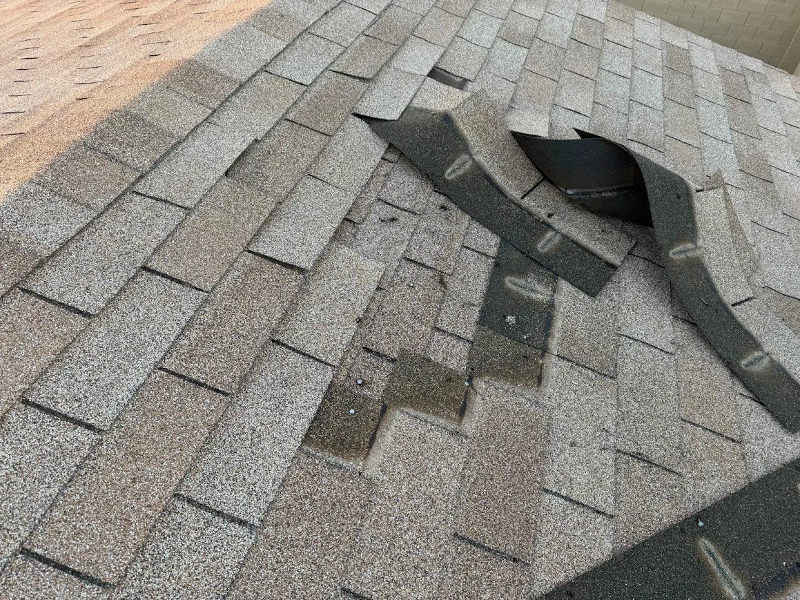 Missing asphalt shingles and exposed roof decking following severe roof damage.