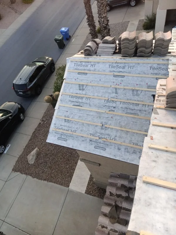 Tile roof underlayment replacement with new underlayment, battens, and tiles staged for reset.