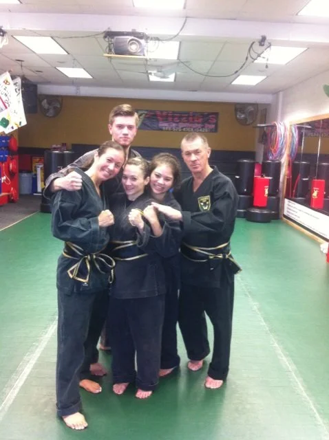 Five Vizzios in martial arts uniforms posing together in a martial arts studio.
