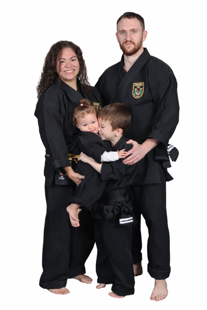 A smiling family of four dressed in martial arts uniforms, standing together with the parents supporting two children, against a plain white background. Johnny and Kitti Vizzio's family.