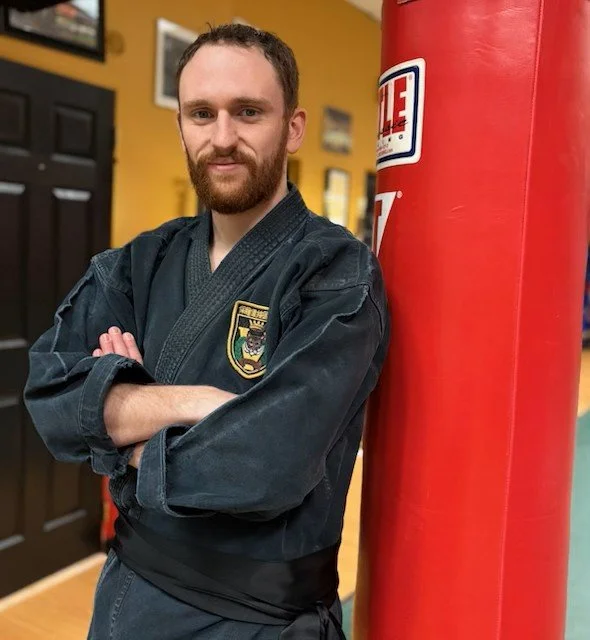 Johnny in a black martial arts uniform standing next to a red punching bag in a gym.