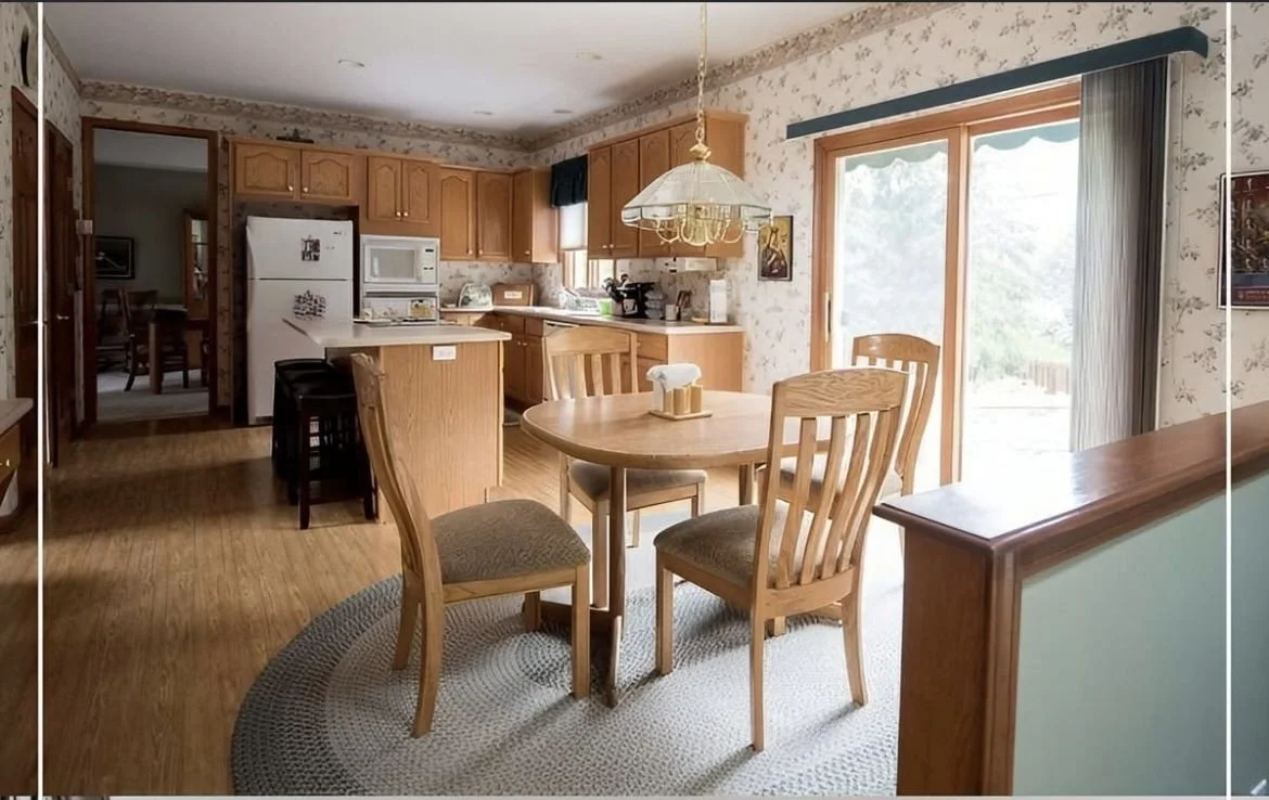 A cozy kitchen and dining area with wooden furniture, a round table with four chairs, a sliding glass door, and a kitchen counter with cabinets, a refrigerator, microwave, and oven.