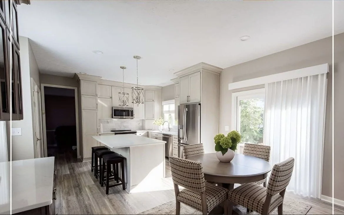 Bright kitchen with white cabinets, stainless steel appliances, an island with seating, and a dining area with a round table and four patterned chairs.