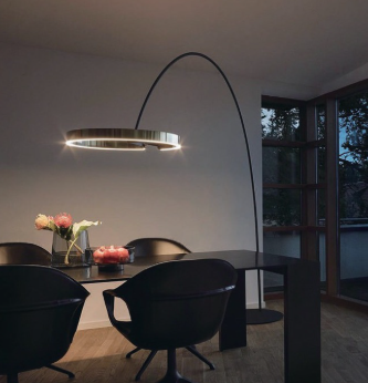 Modern dining room with a black table, black chairs, a floral centerpiece, and a large arched floor lamp. There are windows showing trees outside.
