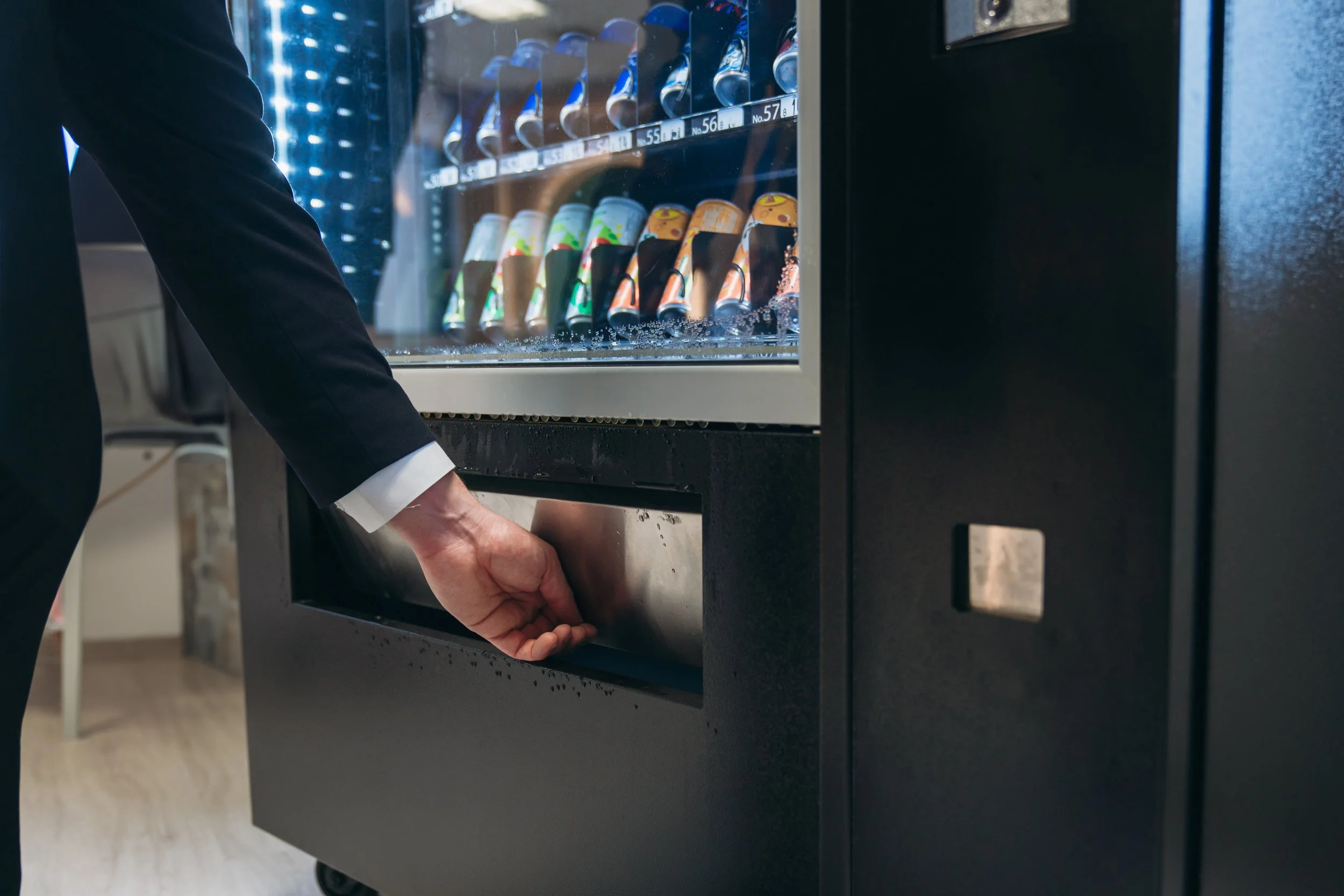 Close-up of a person in a dark suit opening a vending machine filled with snack packets.