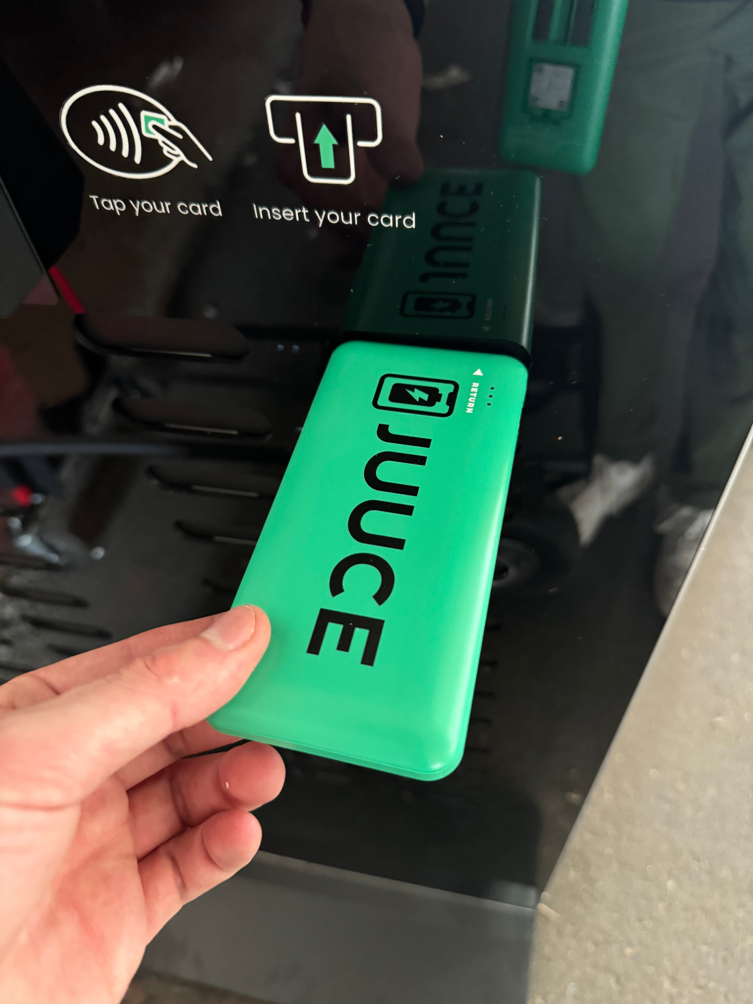 Person holding a green power bank near a contactless card reader with instructions to tap the card or insert the card.