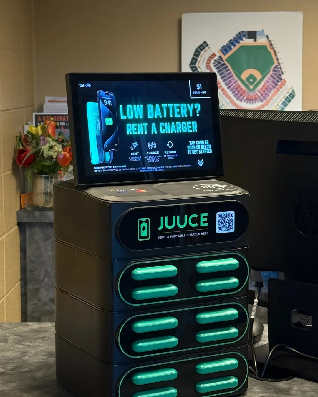 Electric vehicle charging station with a digital screen displaying rent a charger, and a portable charger device labeled JUUCE with a QR code, placed on a counter.