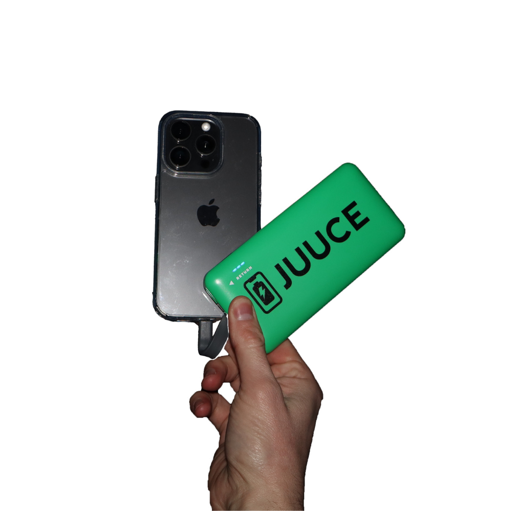 A hand holding a green Juuce charger and an iPhone with a black case against a white background.