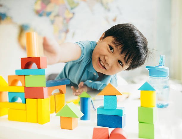 A young boy in a blue shirt playing with colorful building blocks on a white table.