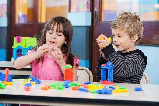Two children playing with colorful plastic building toys at a table.