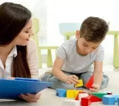 A woman and a boy playing with colorful magnetic building blocks at a table.