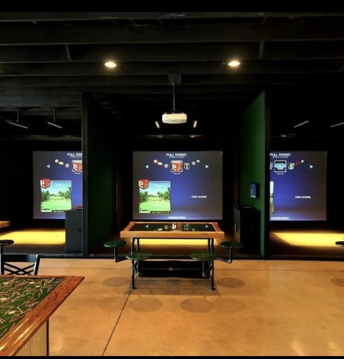 Indoor mini golf course with three simulated golf screens, each with a green landscape background, and a full-swing golf simulator system in the middle.