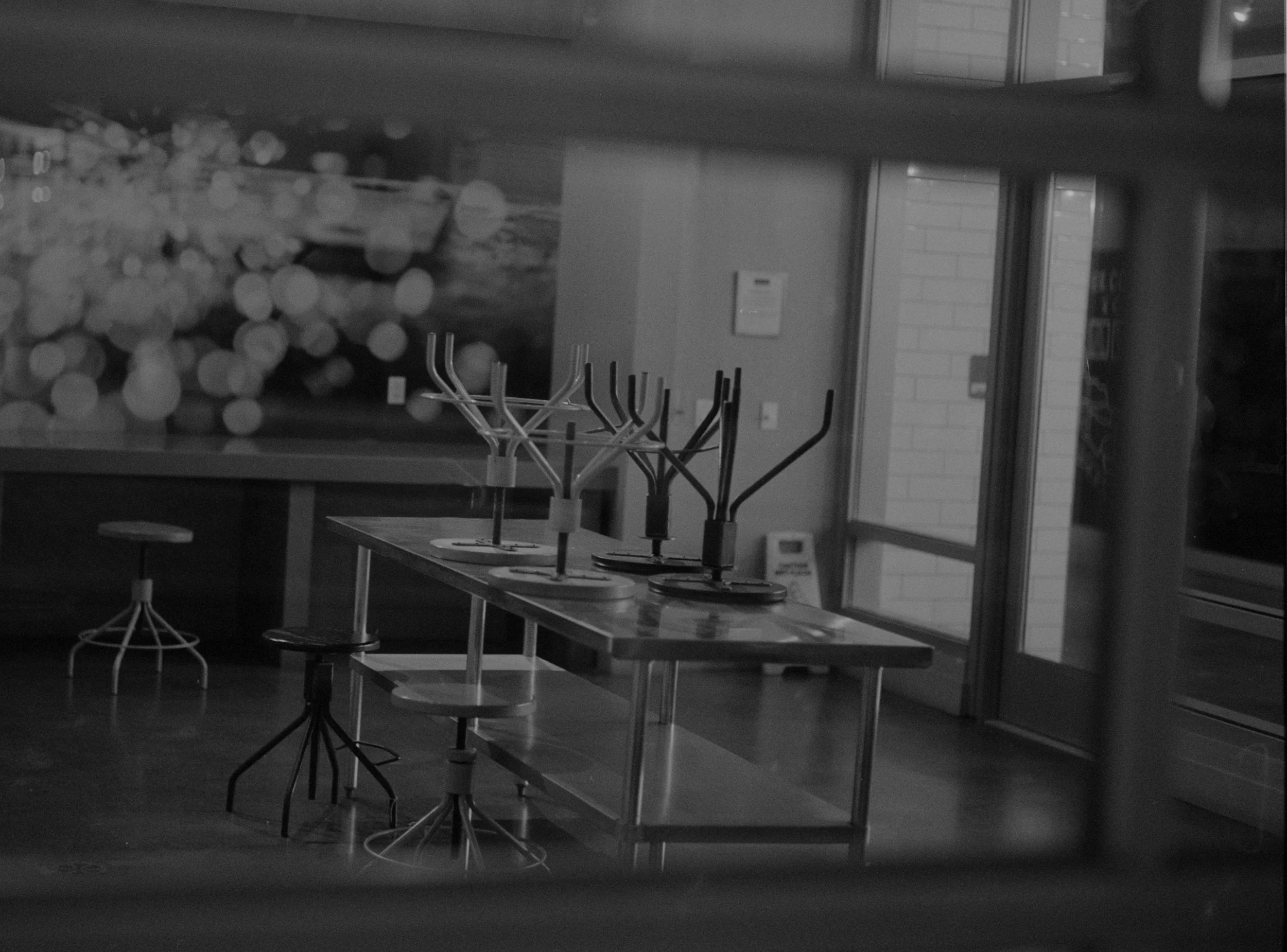 Empty restaurant or cafe with a table holding several coat racks and stools; background features large window and a vending machine.