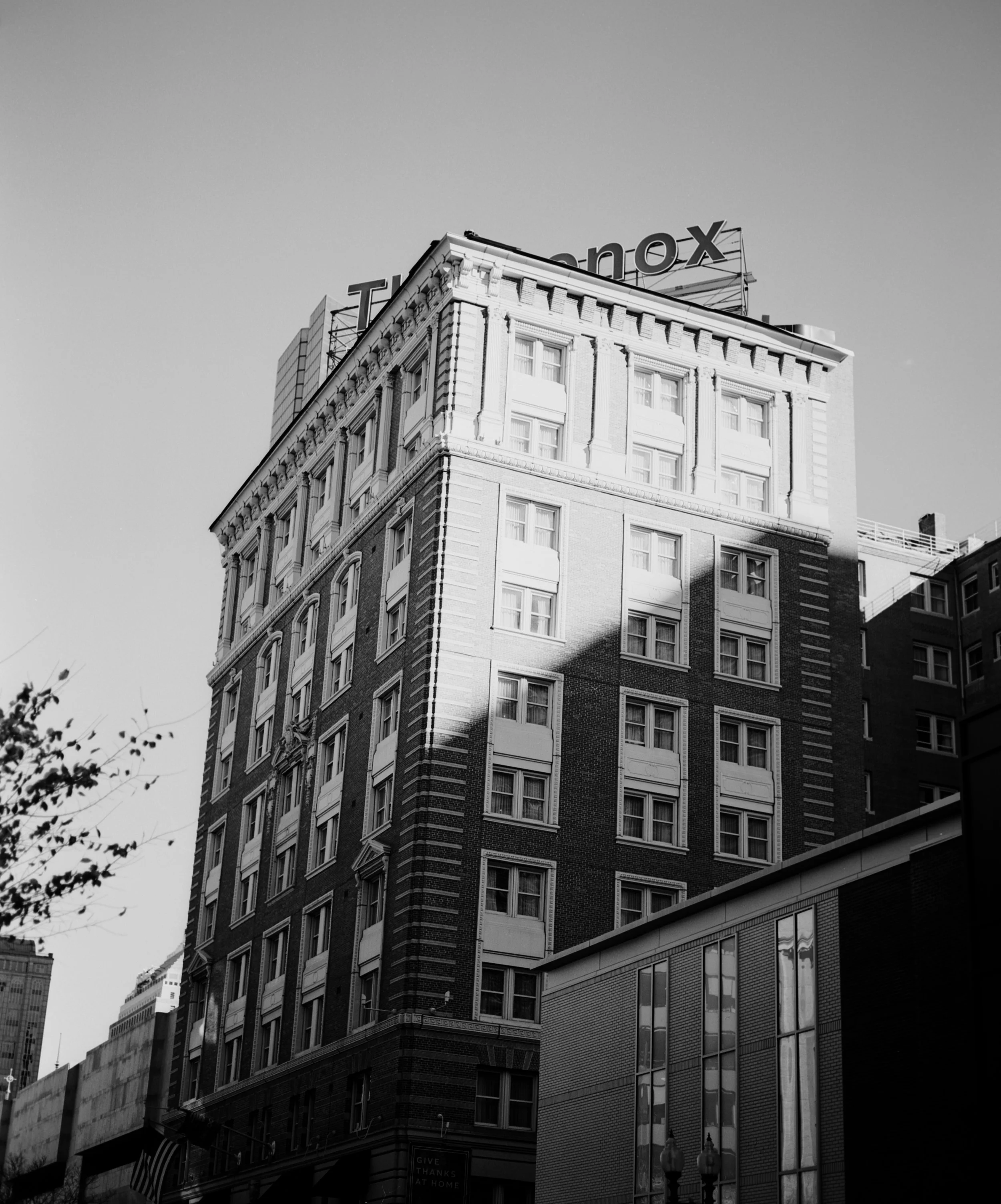 Black and white photo of a tall brick building with multiple windows, casting a shadow on part of the facade, with a sign on the roof reading 'THe Knox'.