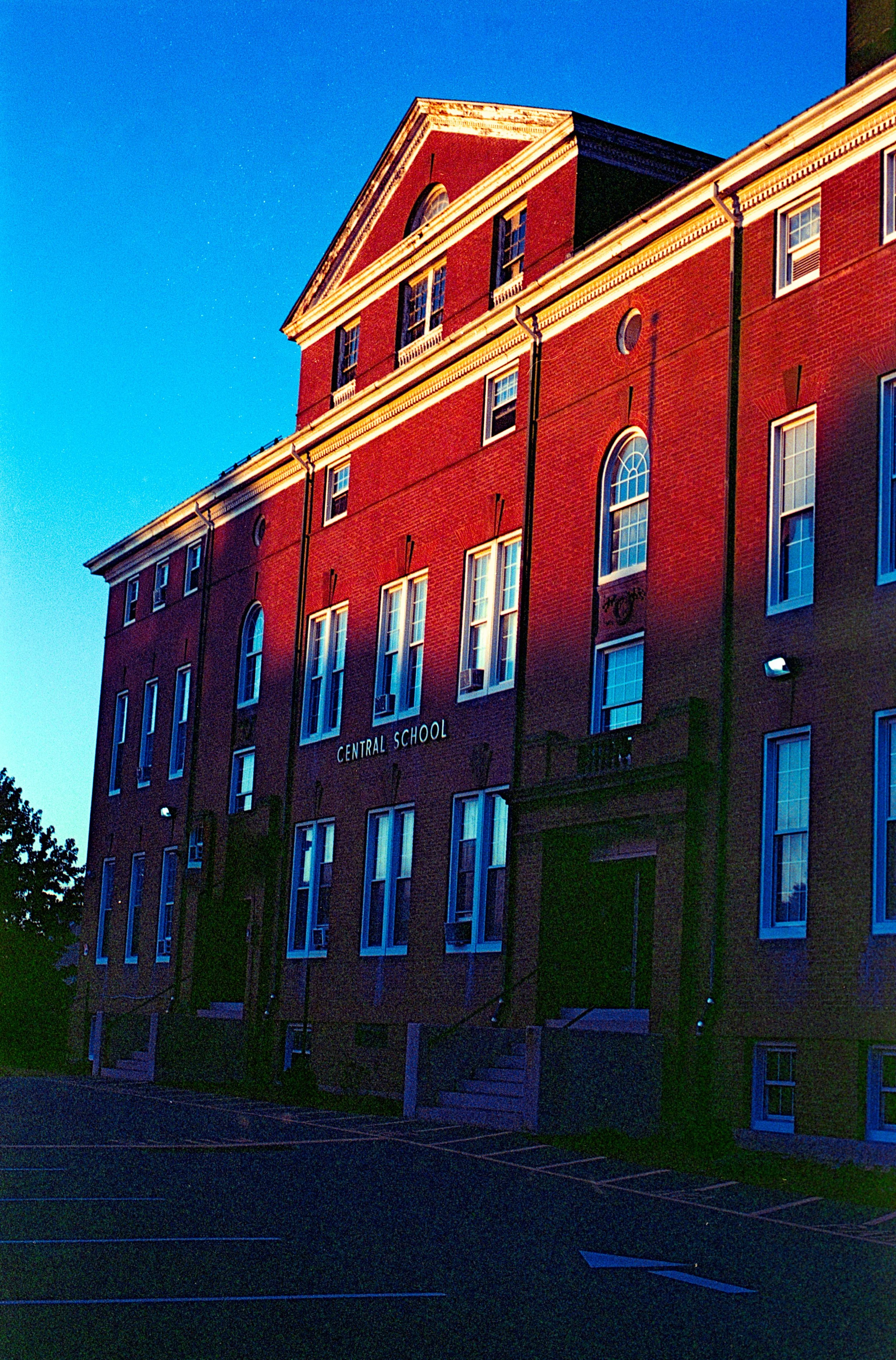 A brick school building with a sign that reads 'Central School' on its facade, under a clear blue sky.