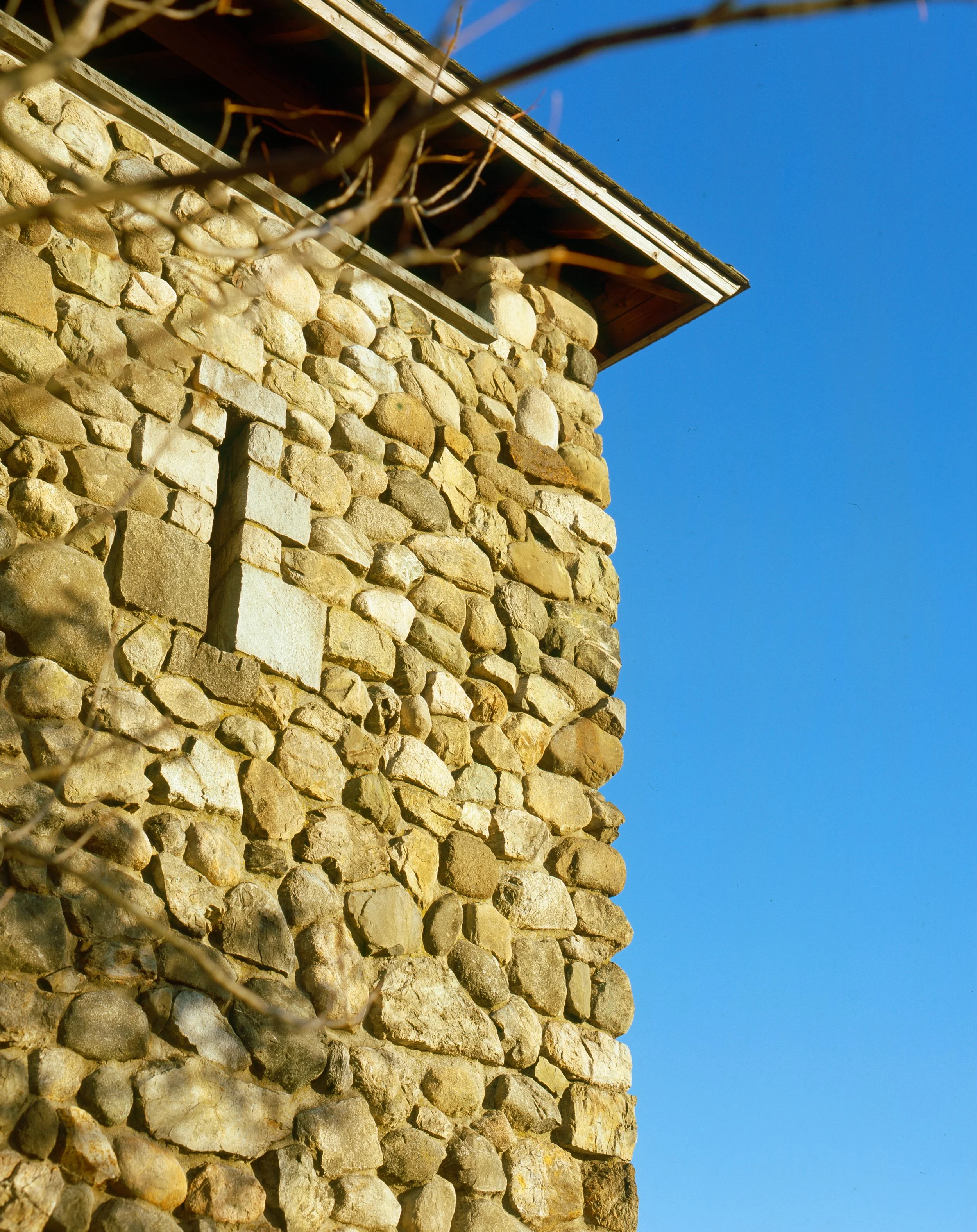 Close-up of a stone chimney on a building with a metal roof, against a clear blue sky.