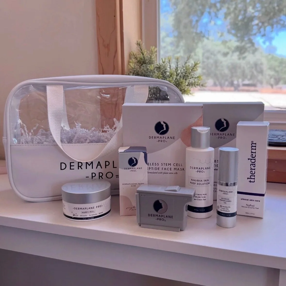 Dermaplane Pro skincare kit including products, a storage bag, and applicator tools on a white surface near a window with trees outside.