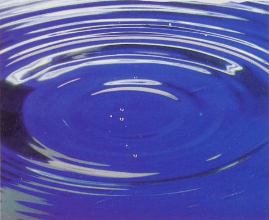 A close-up view of a water droplet creating ripples in a blue body of water.