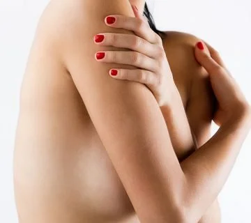 A woman covering her chest with her hands, nail polish on her fingernails, against a plain white background.