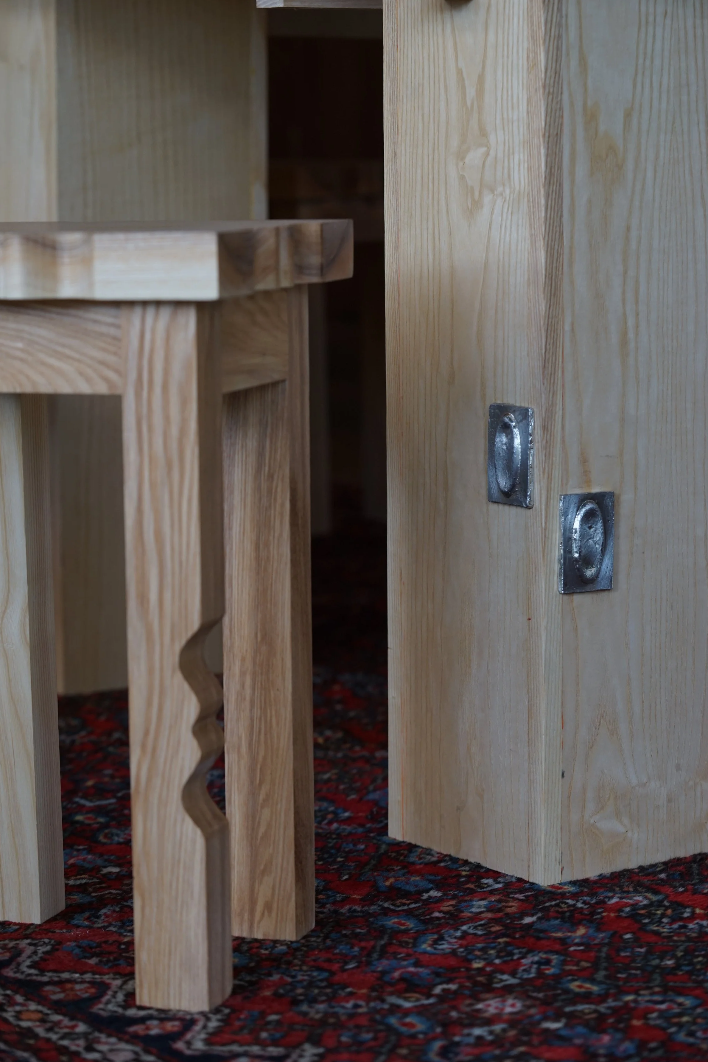 Close-up of unfinished wooden furniture pieces with metal fittings, placed on a colorful patterned carpet.