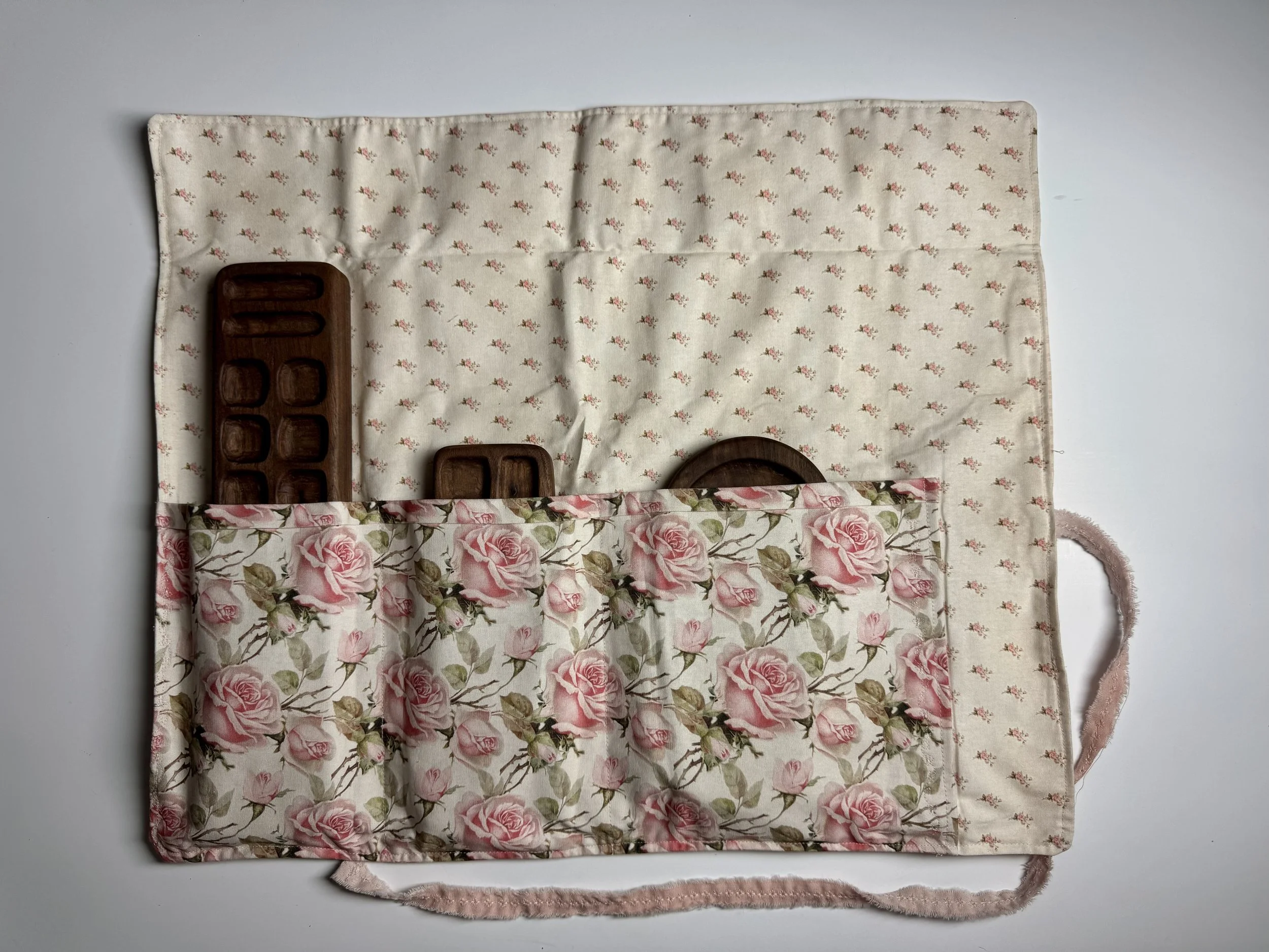 Flat lay of floral-patterned fabric, small wooden tray, and pink knitted item on a white surface.
