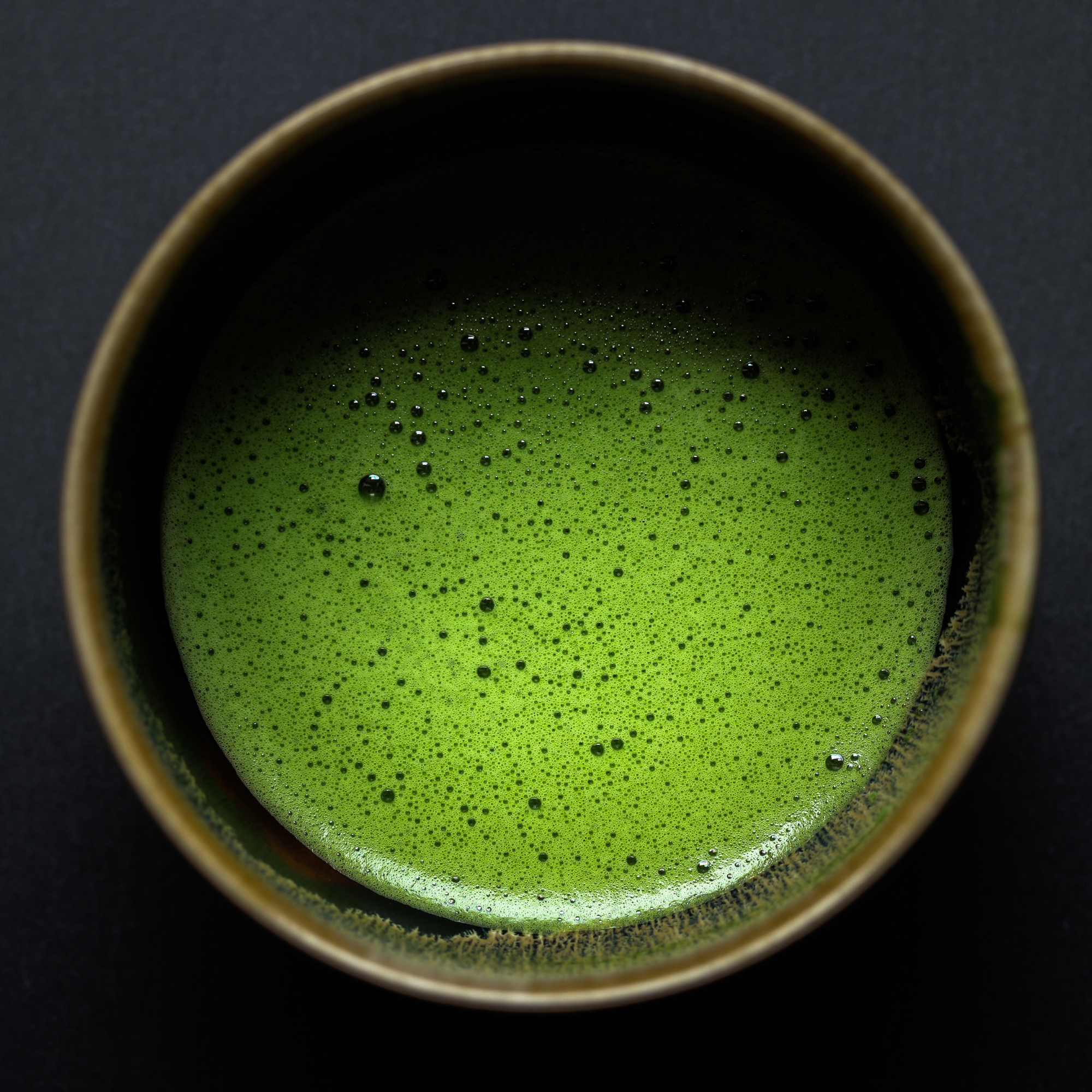 Top view of a cup filled with vibrant green matcha latte with bubbles on the surface.