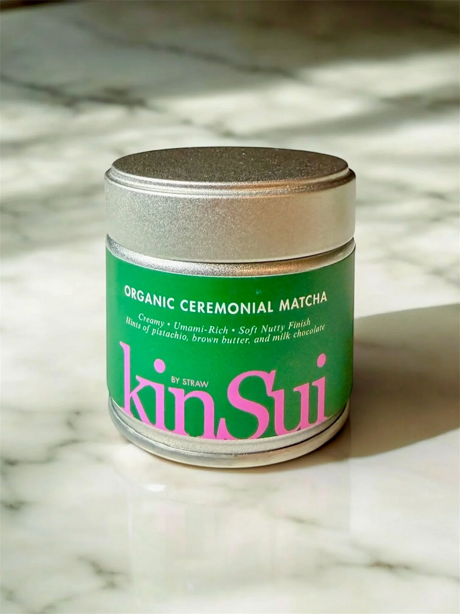 A jar of Kiva lip balm with a green label, silver lid, and pink text, placed on a marble surface.
