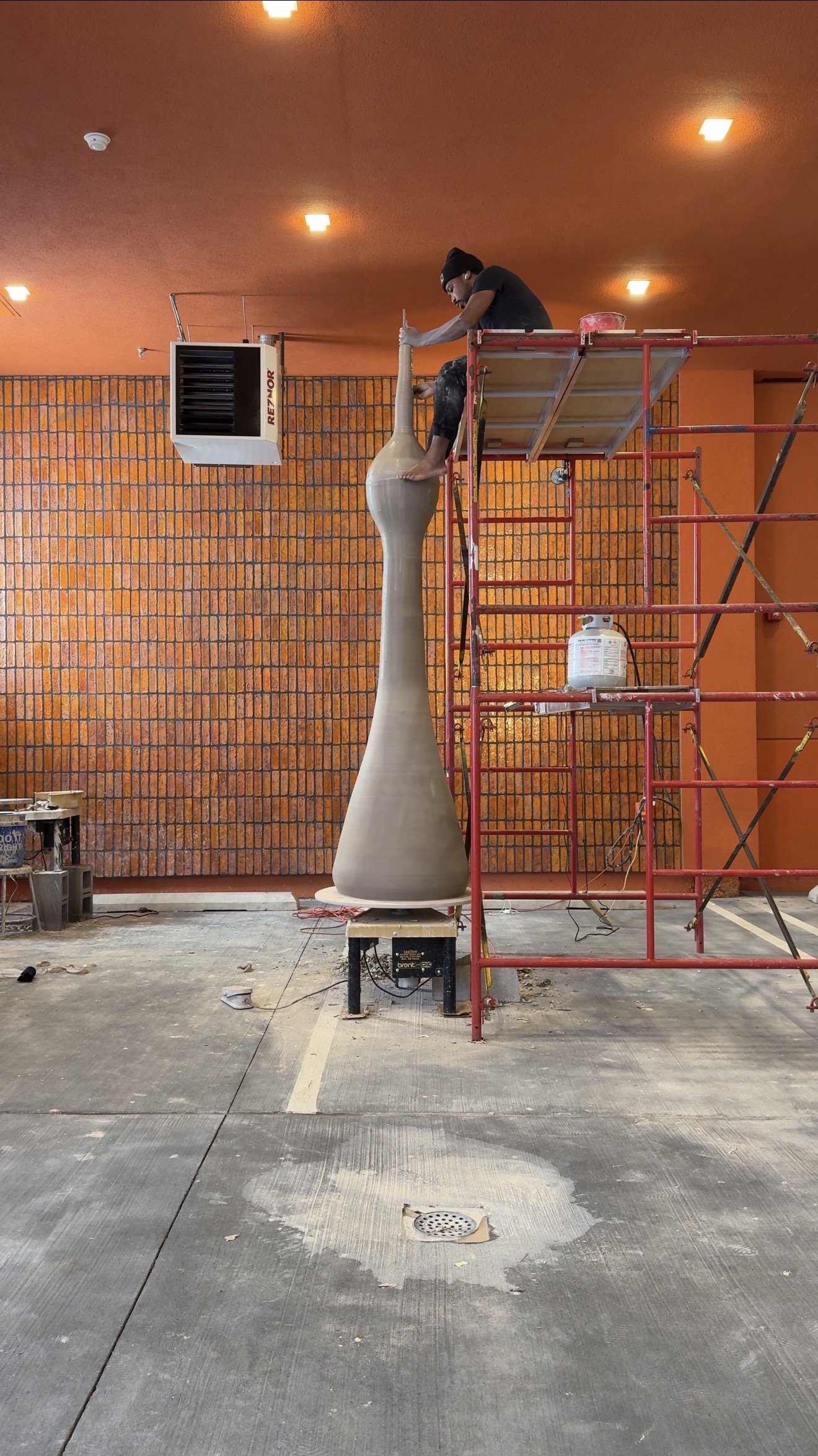Khalil Jannah on scaffolding with a monumental wheel-thrown ceramic monolith (Chasing Giants), studio installation.