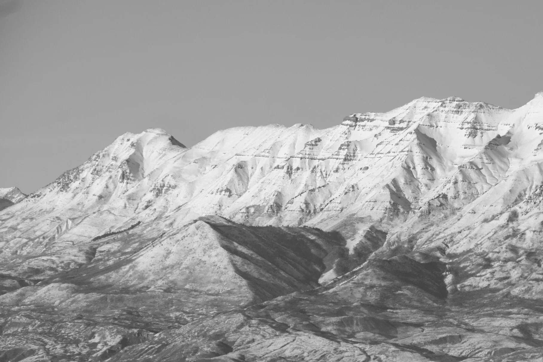 Black and white photograph of snow-covered mountains with rugged terrain and steep slopes.