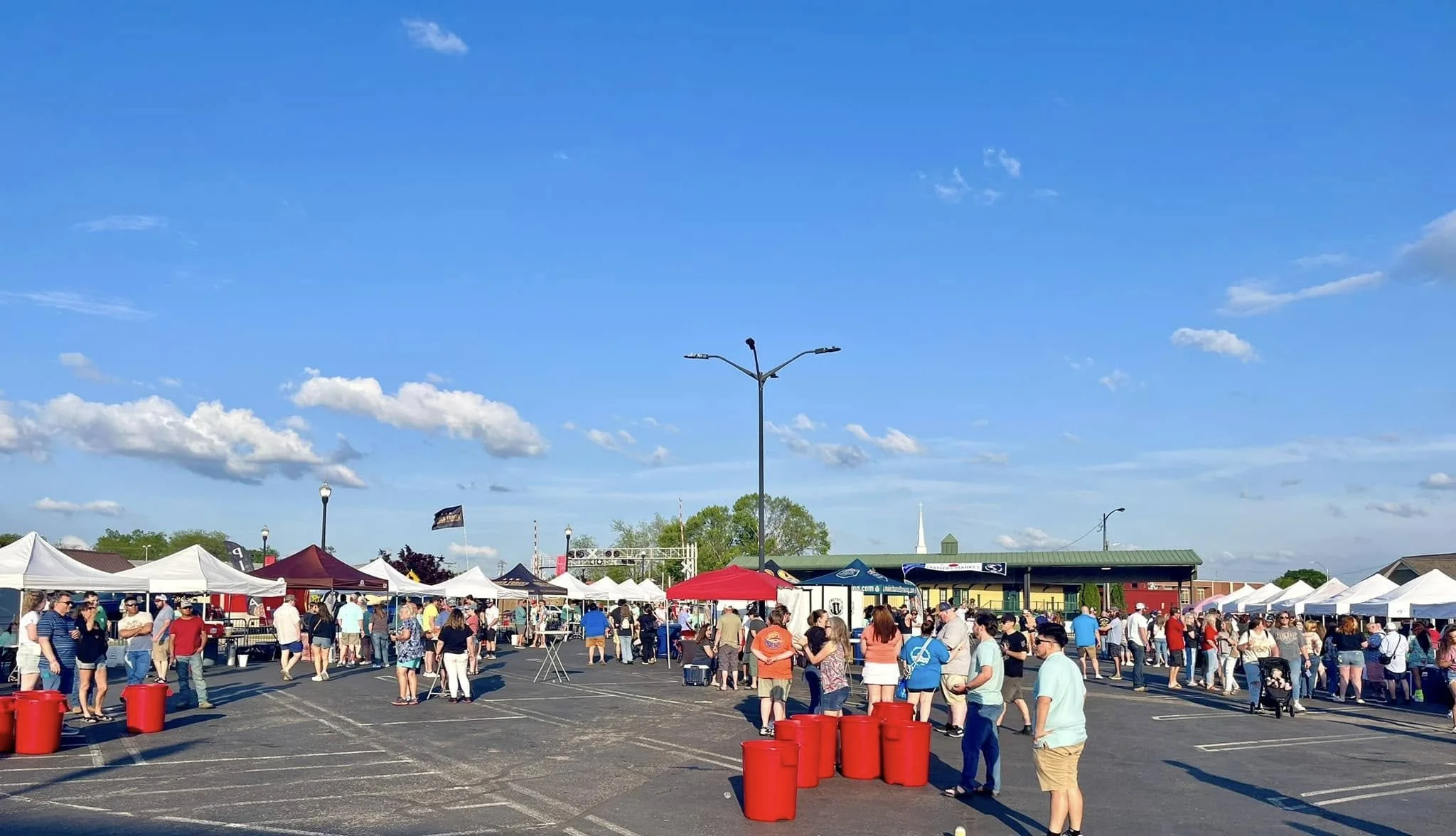 People attending an outdoor event with vendor tents, a stage, and a clear blue sky on a sunny day.