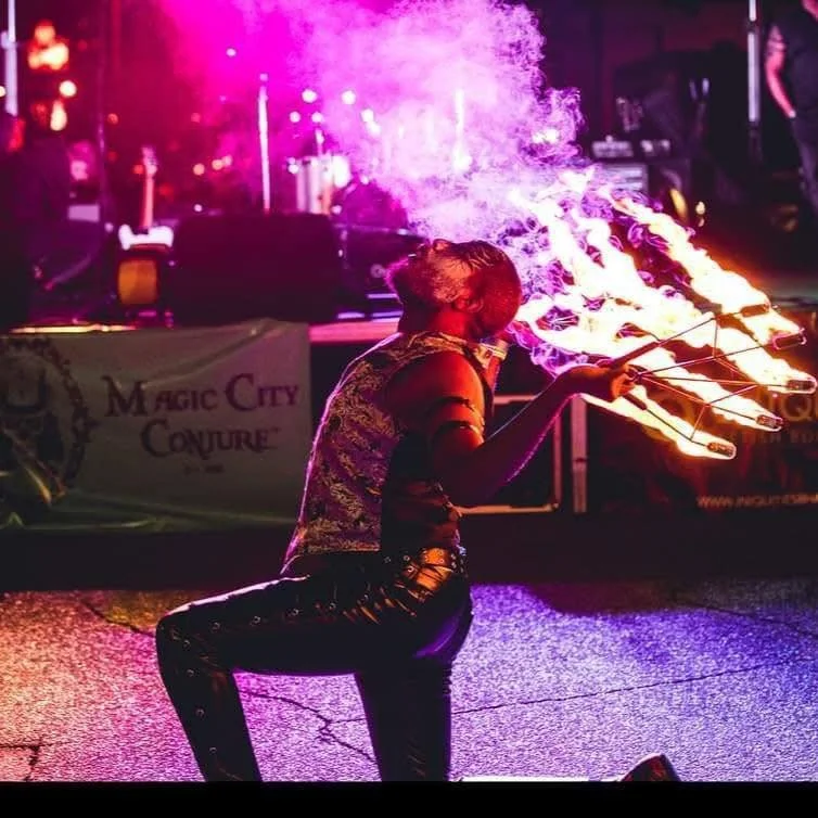 A female fire performer spinning flaming poi at night during a street event.