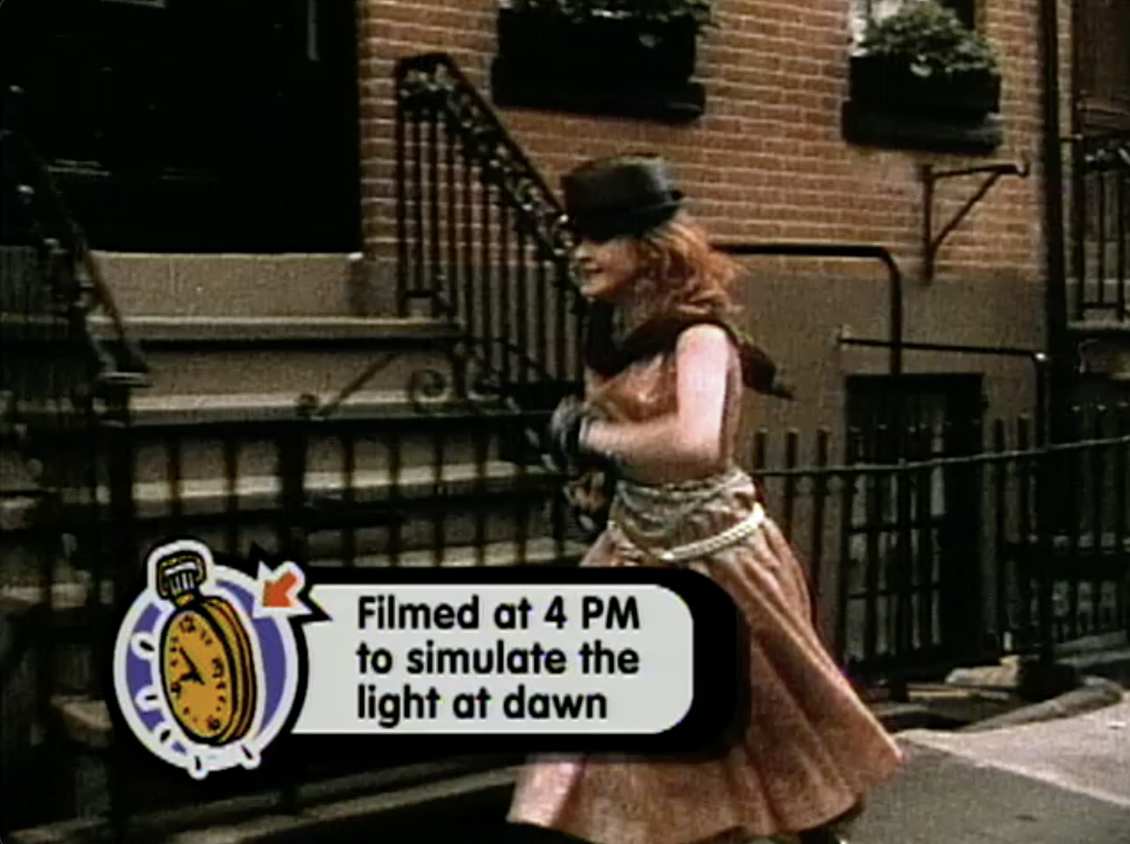 Cyndi Lauper runs in front of a brick building with black gates. There is a graphic of a yellow pocket watch and a speech bubble with the text: 'Filmed at 4 PM to simulate the light at dawn.'