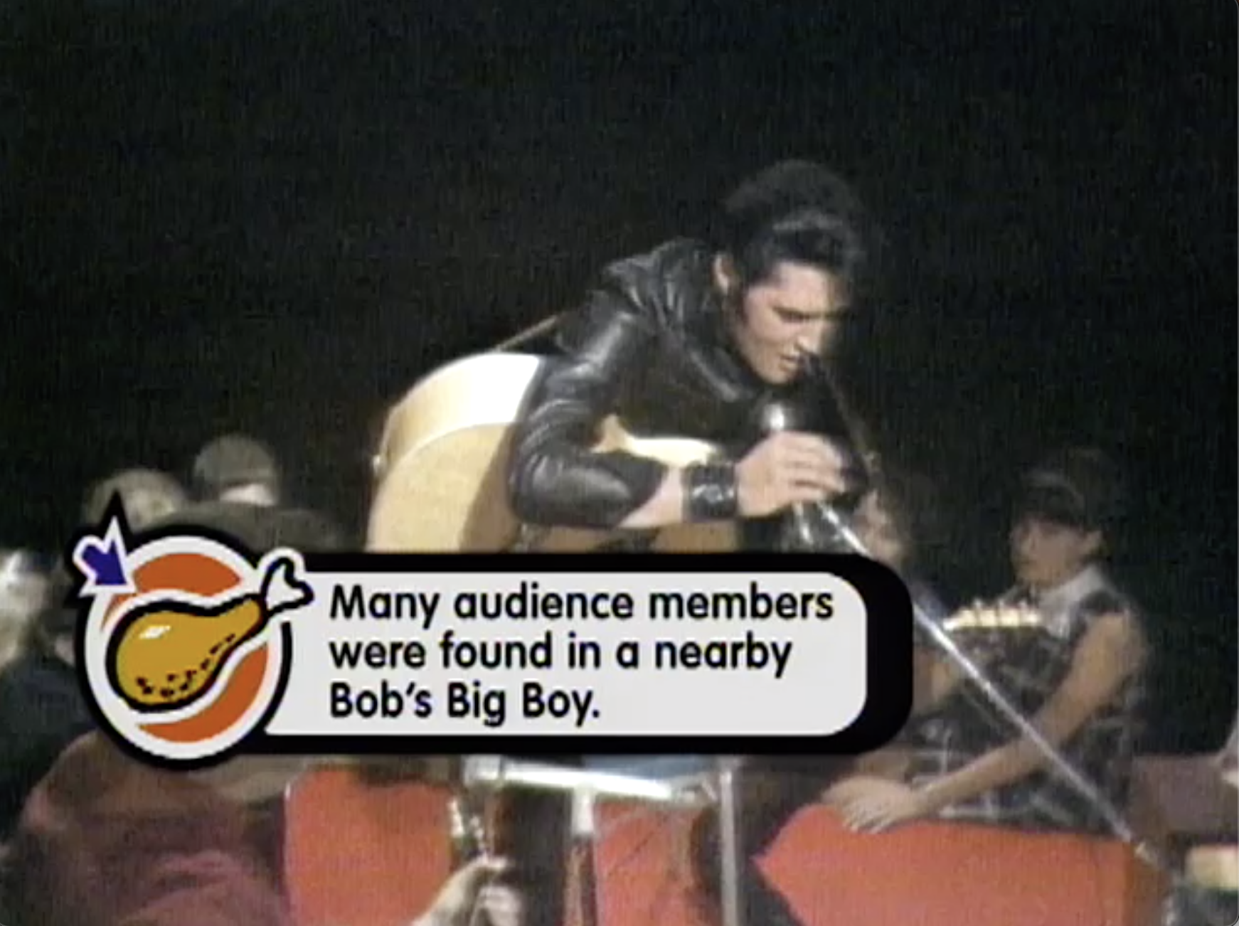 Elvis in a leather jacket sits on a chair, playing an acoustic guitar, in front of a studio audience. A caption with the image of a cartoon fried chicken leg states, 'Many audience members were found in a nearby Bob's Big Boy.'