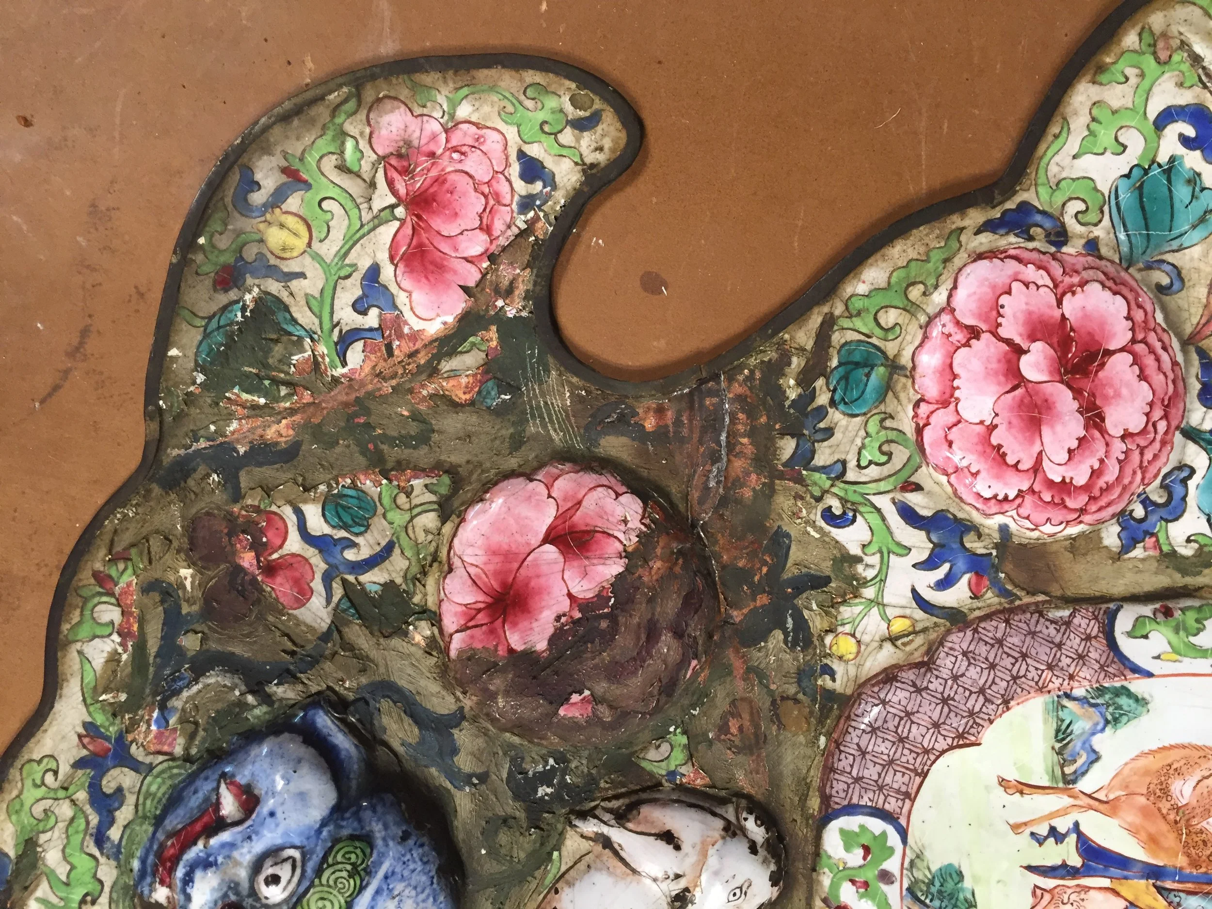 Close-up of a colorful, ornate, ceramic or enamel artifact with floral and animal motifs, showing signs of aging and damage.