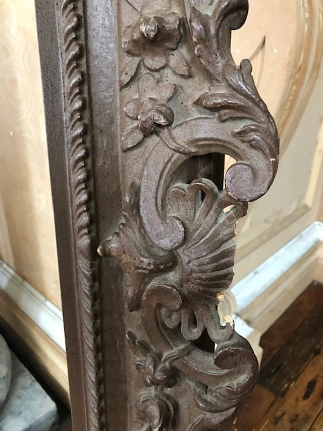 Close-up of an ornate, vintage metal decorative piece with floral and scroll design, possibly part of furniture or a mirror frame.