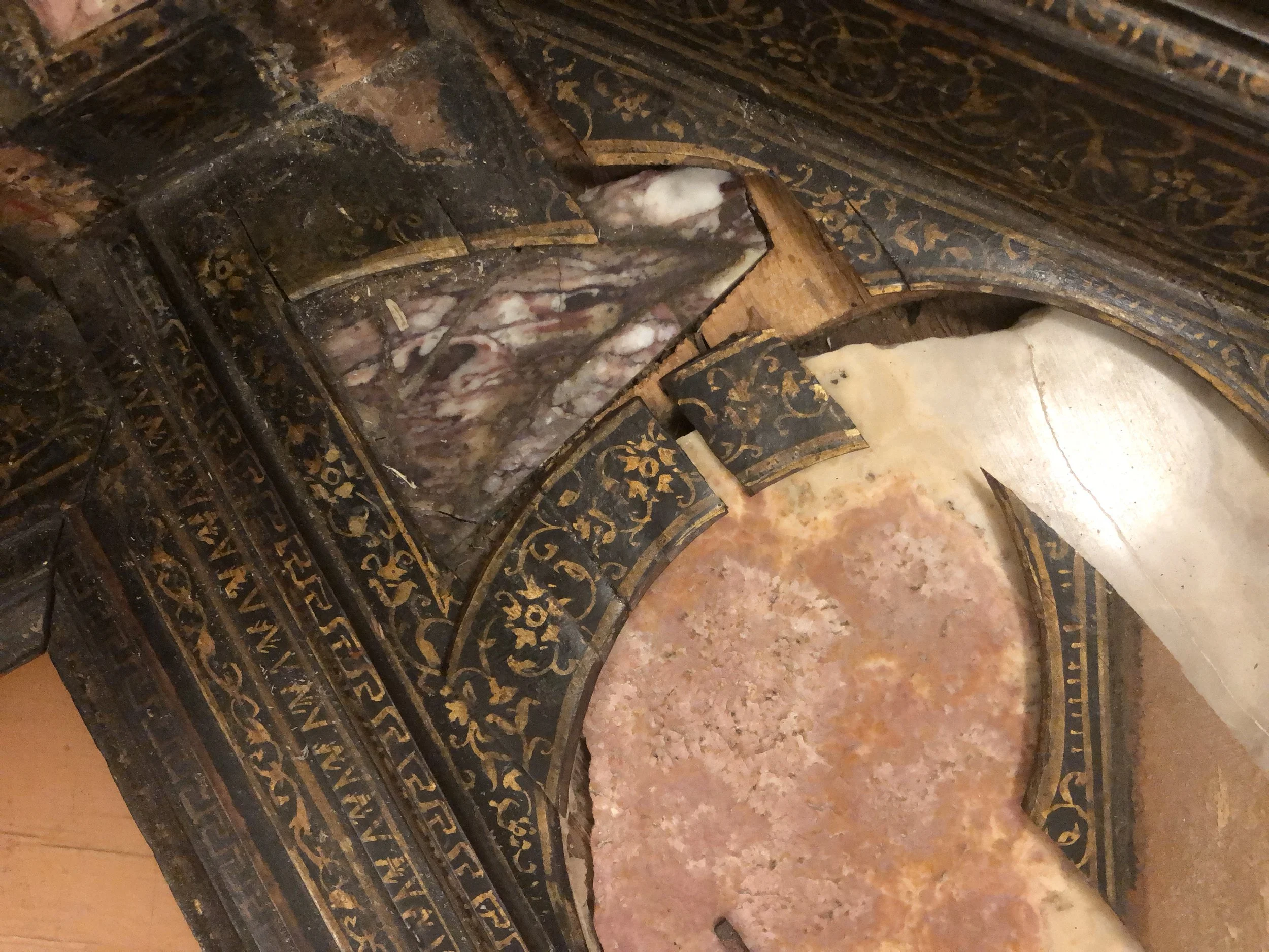 Close-up of damaged, ornate gilded wood and marble surface, possibly part of an antique decorative piece or furniture, with peeling paint and worn details.