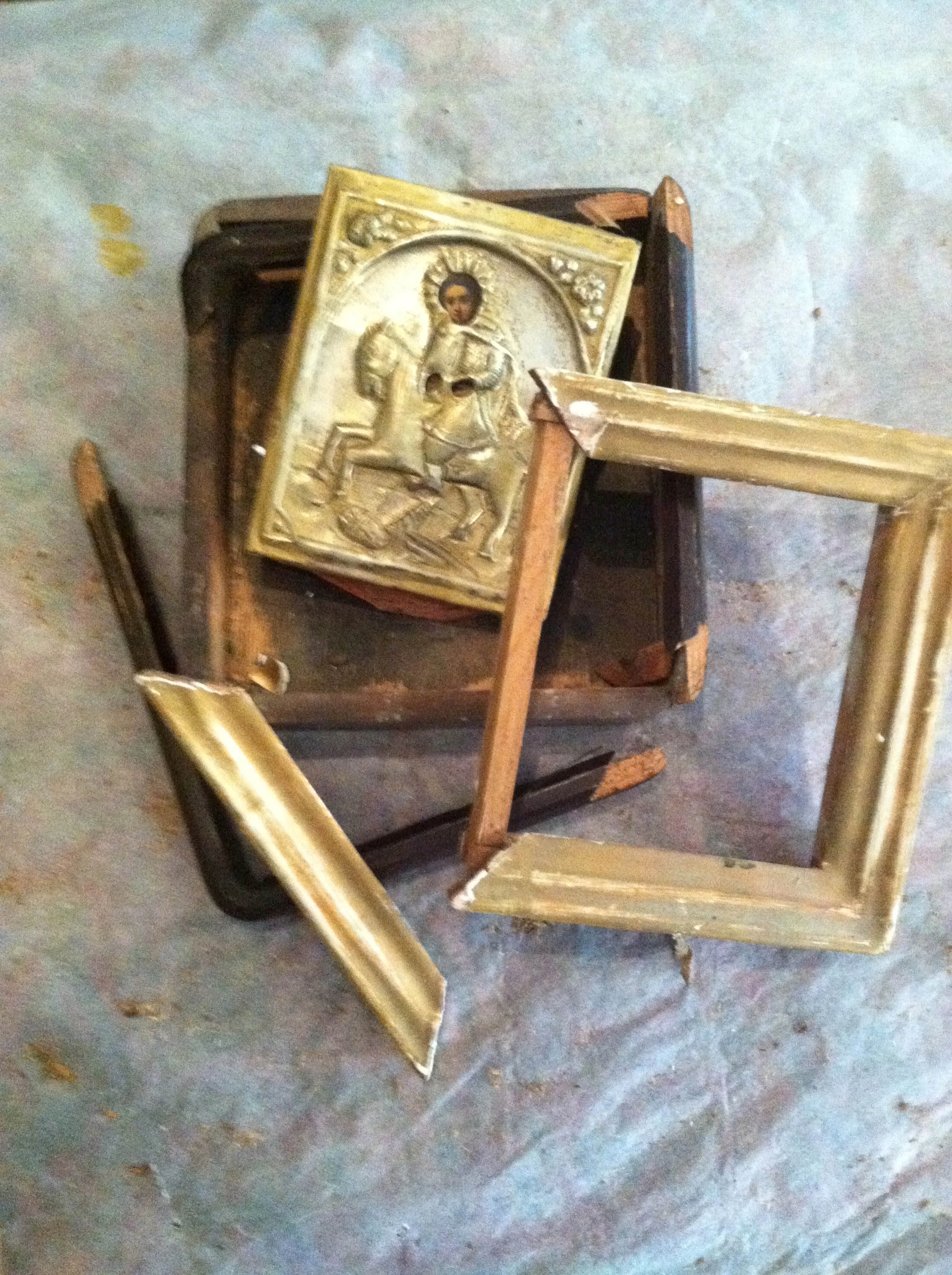 Broken picture frames and a religious icon with a gold frame, placed on an old chair.