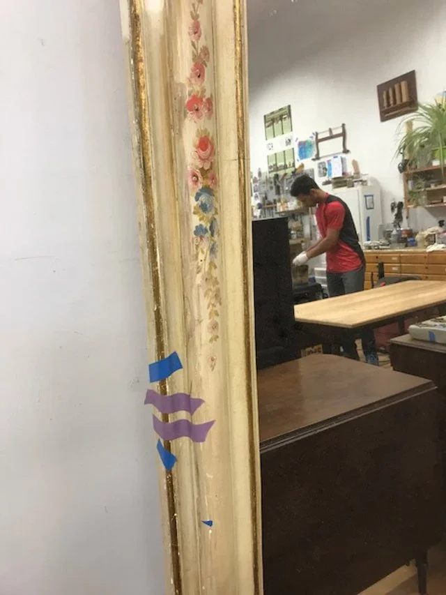 A young man with short hair wearing a red shirt and backpack working at a kitchen counter in a workshop or store with various tools and cabinets visible in the background.