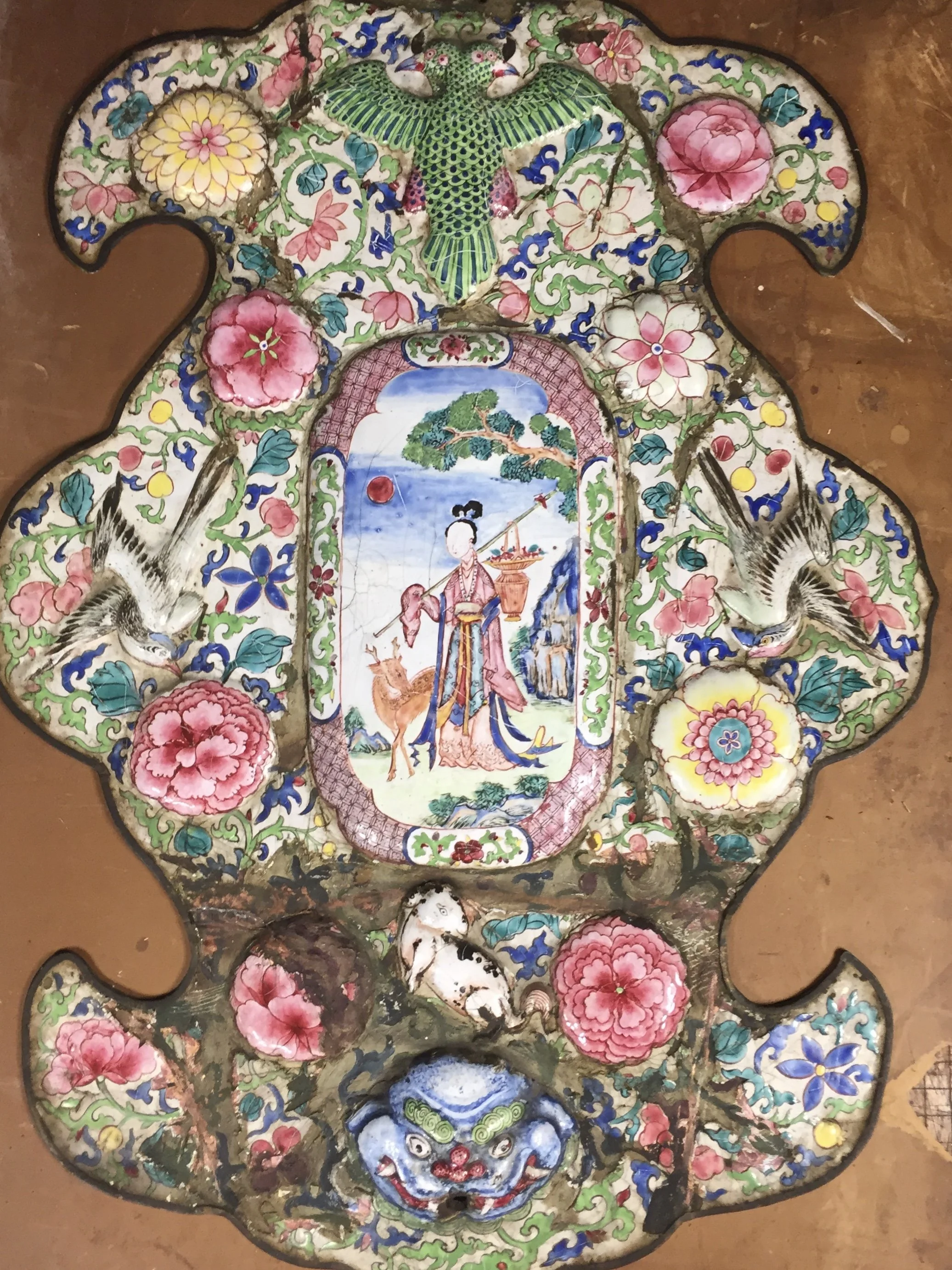 Colorful decorative Asian ceramic or porcelain tray with intricate patterns, floral motifs, birds, and a central painted scene of a woman with a deer in nature, topped with a green bird and a blue and white demon face at the bottom.