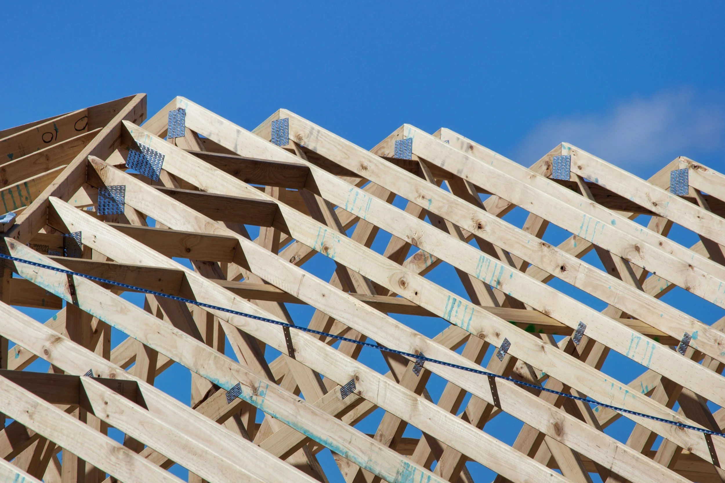 Wooden construction framework for a building under construction, against a bright blue sky.