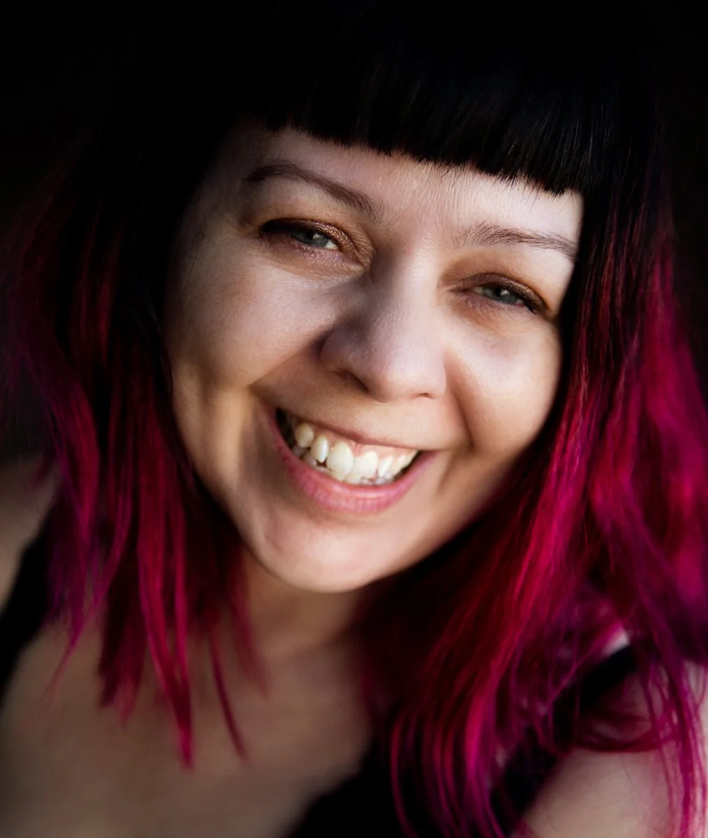Close-up of a woman with black and dark pink hair smiling.