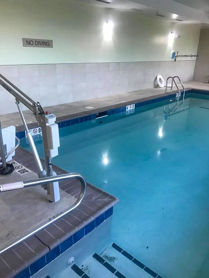 Commercial indoor swimming pool with a ladder, a life preserver, a 'No Diving' sign, and pool depth markings on the wall.
