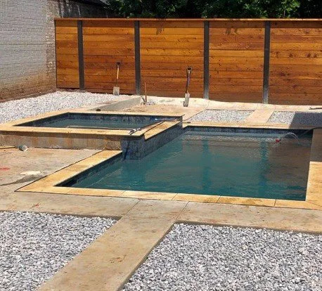 Empty backyard pool with a small attached hot tub, surrounded by a concrete deck and a wooden privacy fence.
