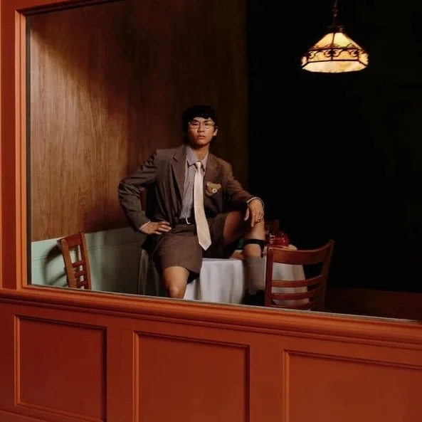 Grentperez posing with one foot on a table inside a dimly lit restaurant. This is the cover of his album 'Backflips in a restaurant'