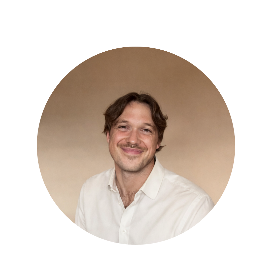 Portrait of a smiling man with brown hair, wearing a light-colored button-up shirt, against a beige background.