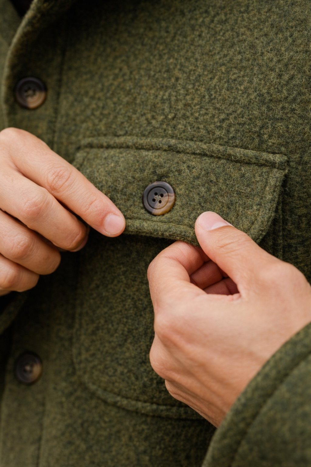 Close-up of a person adjusting the cuff of a green wool coat with brown buttons.